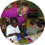 Teacher looking over two preschoolers working on an art project.