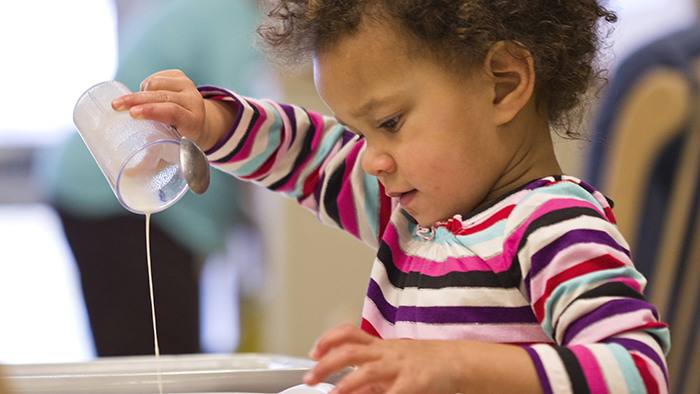 Little boy pouring milk into a bowl.