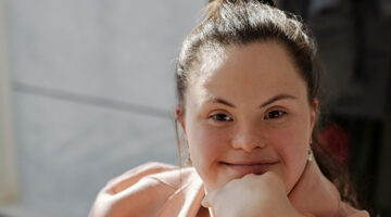 An adult woman with brown hair seated with her chin resting on her hand, smiling at the camera.