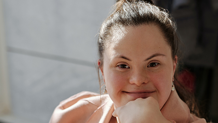 An adult woman with brown hair seated with her chin resting on her hand, smiling at the camera.