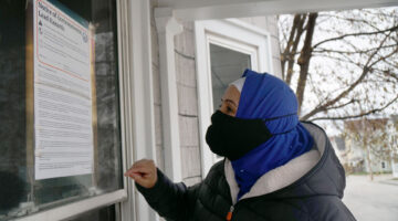 Hibo Omer standing outside a house on Maple Street in Lewiston, Maine, reading an official notice of environmental lead hazards taped to the front door.