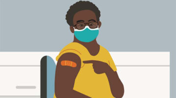 Young woman of color seated, wearing a blue face mask, pointing to a Band-Aid on her right arm after receiving the COVID-19 shot.