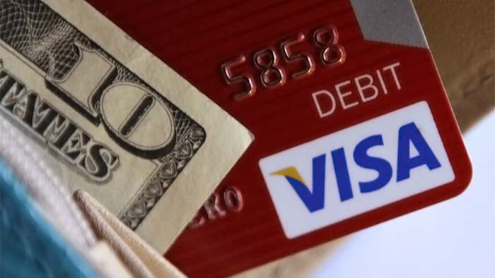 The corners of a U.S. ten-dollar bill and a red VISA debit card sticking out of a blue wallet.