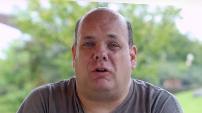 Headshot of Michael Nealey,casually dressed, sitting outdoors and speaking directly to the camera.