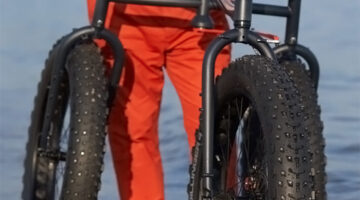 A person with orange pants walking along the shoreline using an Off-Road Afari, a three-wheeled mobility device.
