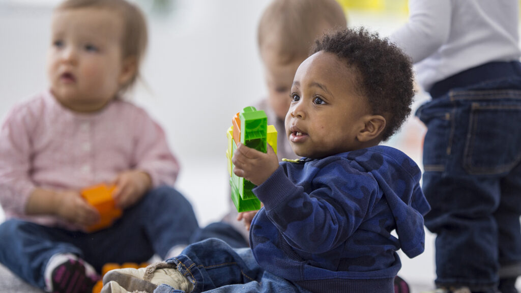 A multi-ethnic group of toddlers are sitting on the floor and are playing together with plastic blocks while on a play date.
