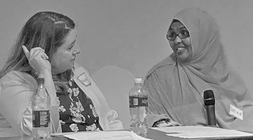 Two women seated at a table participating in a role-playing exercise to explore cultural competence in family-centered care. Please read the post content below.