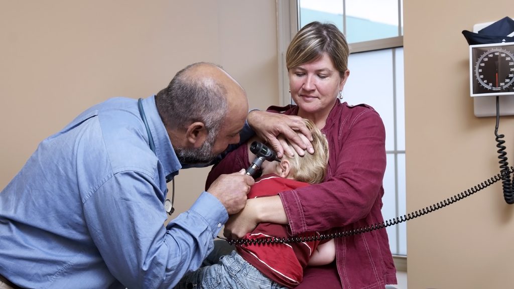 A mother holding onto her child as a doctor looks in his ears.