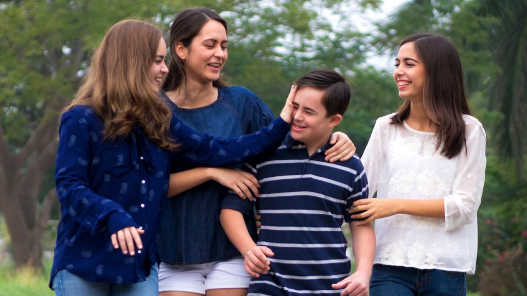Three young adult women smiling and looking at their younger brother.