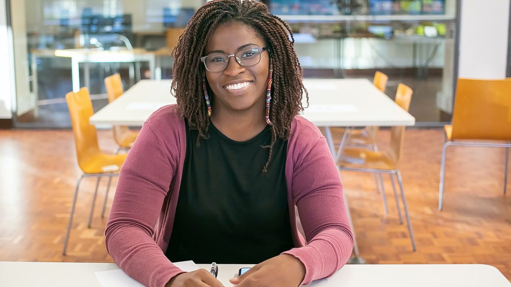 Female dark skinned student sitting at a table in the cafeteria.