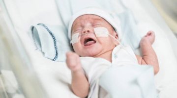 Beautiful premature baby boy in an incubator at neonatal intensive care unit with oxygen crying.