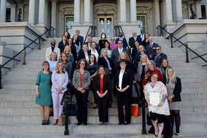 Group photo of 37 adults, men and women, standing outside on the front steps of the Eisenhower Executive Office Building in Washington, DC.